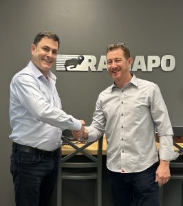 Two men shaking hands in front of a rapapo sign.